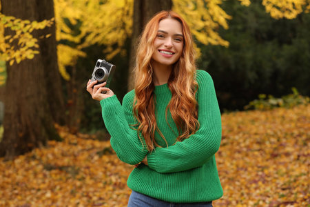 Smiling woman with camera in autumn parkの写真素材