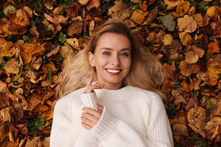 Smiling woman lying among autumn leaves outdoors, top viewの写真素材