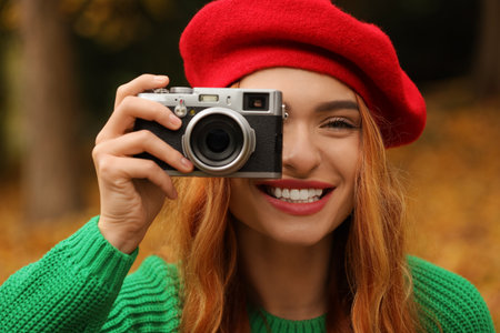 Smiling woman with camera taking photo in autumn parkの写真素材