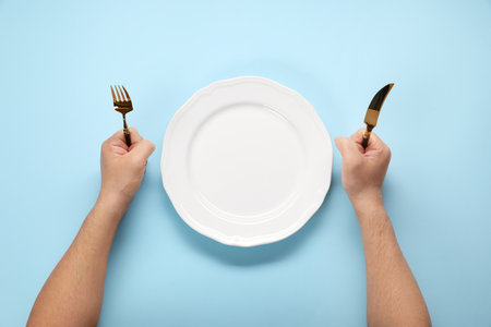 Man with cutlery and empty plate at light blue table, top viewの写真素材
