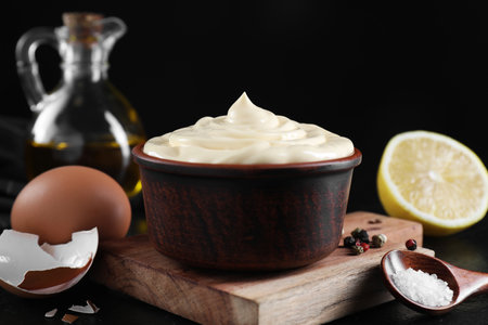 Fresh mayonnaise sauce in bowl and ingredients on black table, closeupの写真素材