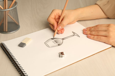 Woman drawing glass of wine with graphite pencil at light wooden table, closeupの写真素材