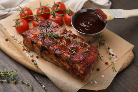 Tasty roasted pork ribs served with thyme, sauce and tomatoes on wooden table, closeupの写真素材