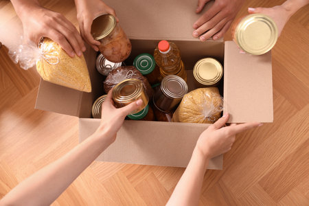 Group of volunteers packing food products at wooden table, top viewの写真素材
