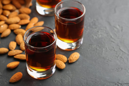 Glasses with tasty amaretto liqueur and almonds on dark gray table, closeup. Space for textの写真素材