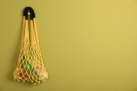 Conscious consumption. Net bag with eco friendly products hanging on olive wall, space for textの写真素材