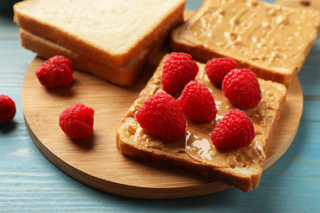 Delicious toasts with peanut butter and raspberries on light blue wooden table, closeupの写真素材