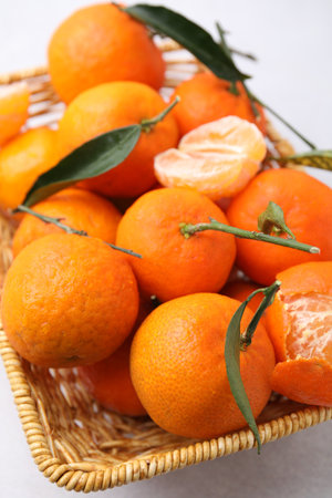 Fresh ripe tangerines with green leaves in wicker basket on white table, closeupの写真素材