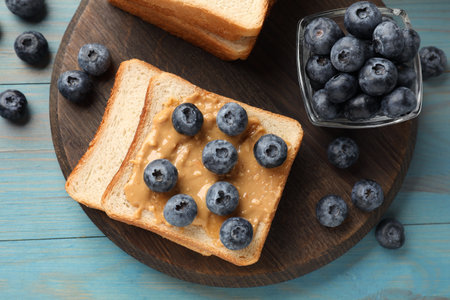 Delicious toasts with peanut butter and blueberries on light blue wooden table, top viewの写真素材