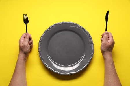 Man with fork, knife and empty plate at yellow table, top viewの写真素材