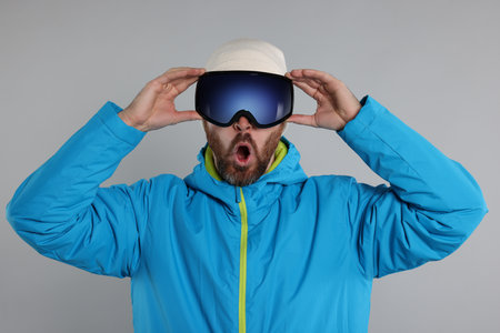 Winter sports. Emotional man in ski suit and goggles on gray backgroundの写真素材