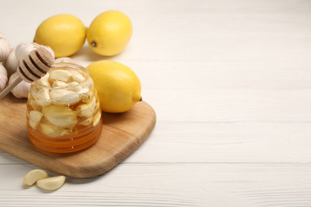 Honey with garlic in glass jar, lemons and dipper on white wooden table. Space for textの写真素材