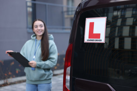 Instructor with clipboard near car outdoors, selective focus on L-plate. Driving schoolの写真素材