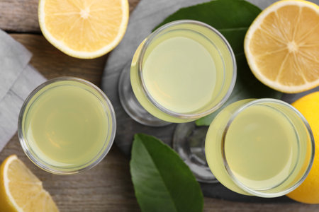 Tasty limoncello liqueur, lemons and green leaves on wooden table, top viewの写真素材