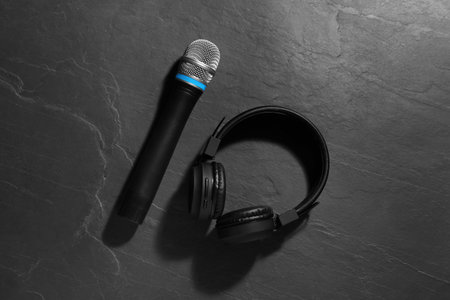 Microphone and headphones on gray textured background, flat lay. Sound recording and reinforcement