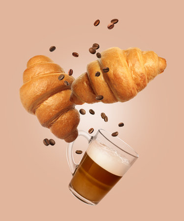 Fresh croissants, aromatic coffee and roasted beans in air on peach color backgroundの写真素材