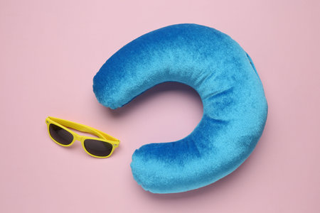 Light blue travel pillow and sunglasses on pink background, flat lay