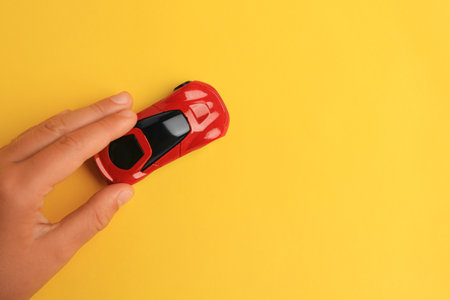 Child playing with toy car on yellow background, top view. Space for text
