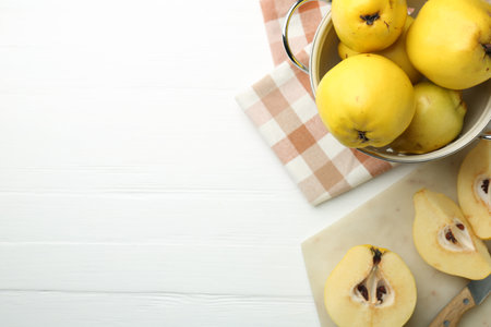Tasty ripe quinces, metal colander and knife on white wooden table, flat lay. Space for textの写真素材
