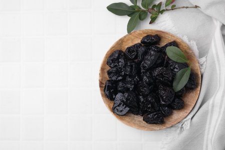 Sweet dried prunes and green leaves on white tiled table, top view. Space for textの写真素材