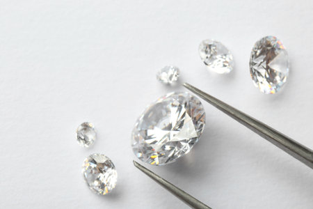 Tweezers with beautiful shiny diamonds on white background, flat lay. Space for textの写真素材