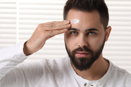 Man with dry skin applying cream onto his forehead indoorsの写真素材