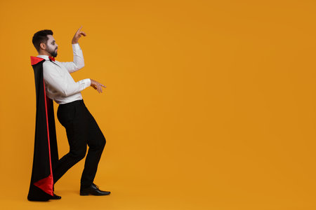 Man in scary vampire costume with fangs posing on orange background, space for text. Halloween celebrationの写真素材