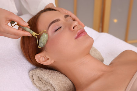 Young woman receiving facial massage with jade roller in beauty salon, closeupの写真素材