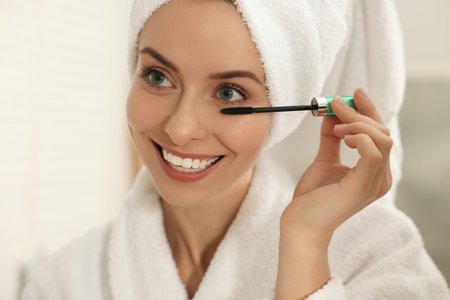 Beautiful woman applying mascara with brush indoors, closeup