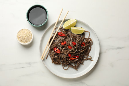 Tasty buckwheat noodles (soba) with chili pepper and lime served on white marble table, flat layの写真素材