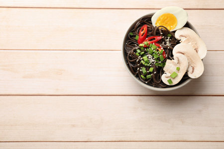 Tasty buckwheat noodles (soba) with mushrooms, egg and chili pepper in bowl on wooden table, top...