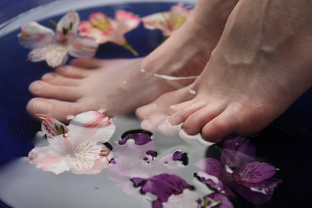 Woman soaking her feet in bowl with water and flowers, closeup. Spa treatmentの写真素材