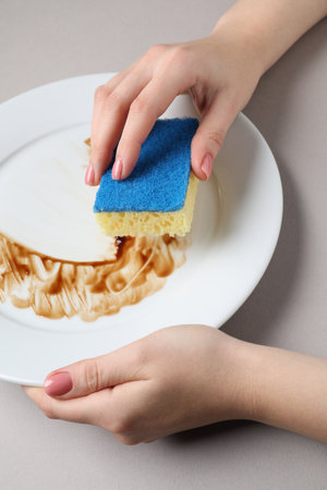 Woman washing dirty plate with sponge on light gray background, closeupの写真素材