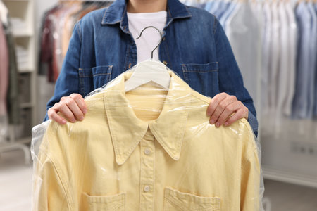 Dry-cleaning service. Woman holding shirt in plastic bag indoors, closeupの写真素材