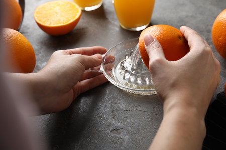 Woman squeezing orange juice at gray table, closeup