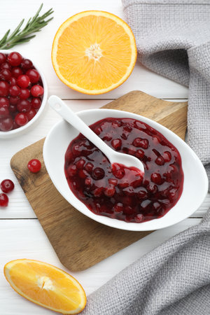 Tasty cranberry sauce in bowl, fresh berries and orange slices on white wooden table, flat layの写真素材