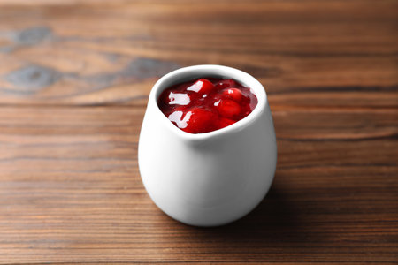 Fresh cranberry sauce in pitcher on wooden table, closeup