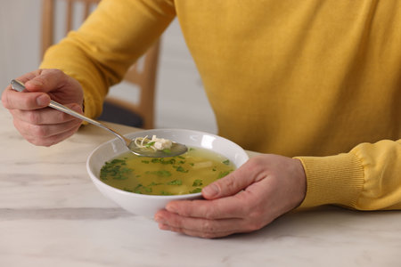 Man eating delicious chicken soup at light marble table indoors, closeupの写真素材