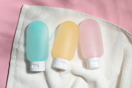 Cosmetic travel kit and towel on pink background, top view. Bath accessories