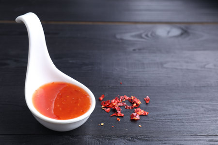 Chili sauce in spoon on black wooden table, closeup. Space for textの写真素材