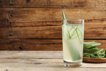 Tasty aloe juice in glass and cut fresh leaves on wooden table, space for textの写真素材