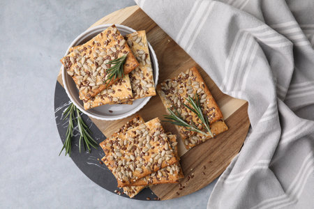 Cereal crackers with flax, sunflower, sesame seeds and rosemary on gray table, top view