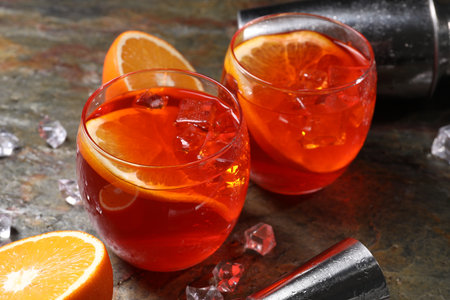 Aperol spritz cocktail, ice cubes and orange slices in glasses on gray textured table, closeupの写真素材