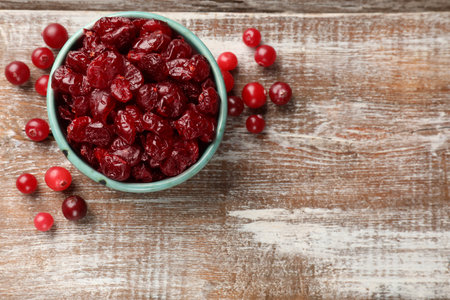 Tasty dried cranberries in bowl and fresh ones on rustic wooden table, top view. Space for textの写真素材