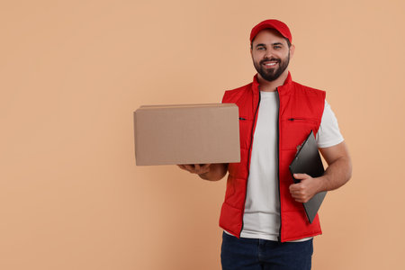 Happy young courier with parcel and clipboard on light brown background. Space for textの写真素材