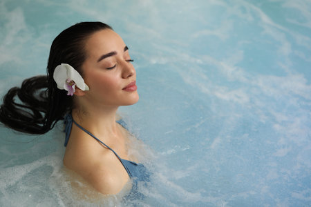 Beautiful woman with orchid flower in spa swimming pool, space for text