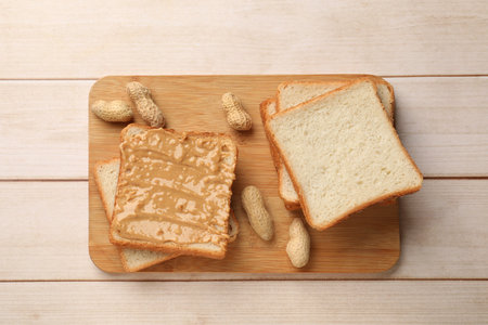 Delicious toasts with peanut butter and nuts on light wooden table, top view