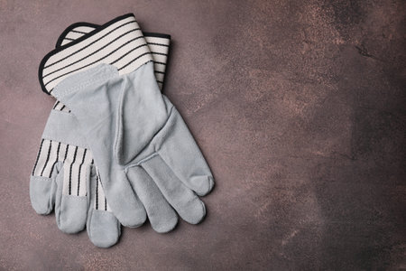 Pair of color gardening gloves on brown textured table, top view. Space for text