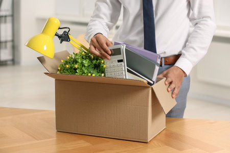 Unemployment problem. Man with box of personal belongings at table in office, closeup