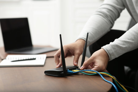 Man inserting cable into Wi-Fi router at wooden table indoors, closeupの写真素材